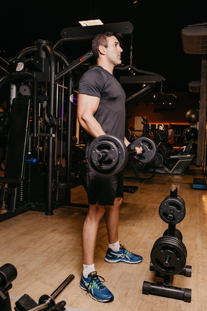 Fit adult man in gym performing weightlifting workout with dumbbells.