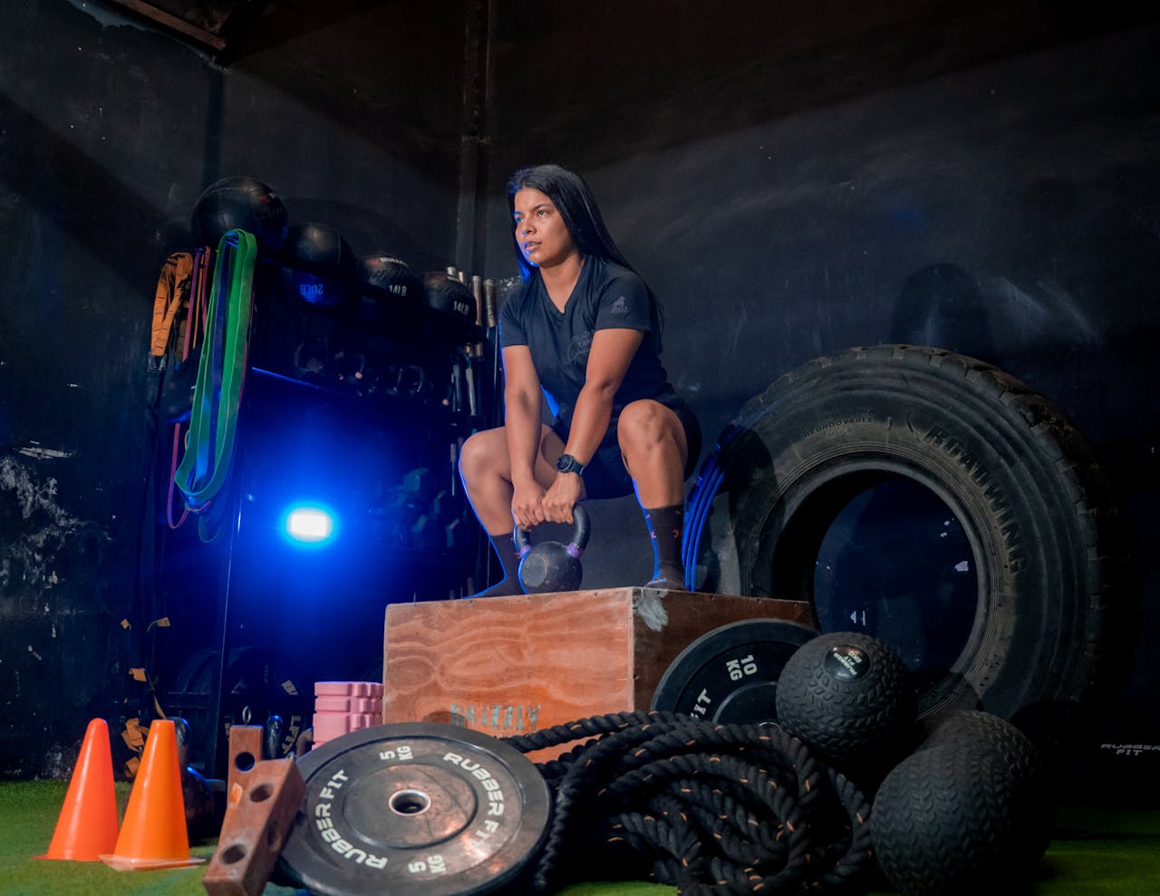 A woman squats with a kettlebell in a gym setting, focusing on strength training.